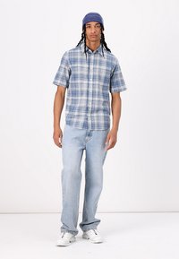 Korte mouw overhemd met knopen in blauwe tartan, gecombineerd met lichtblauwe jeans en witte sneakers. Geaccessoreerd met een blauwe breibarret.