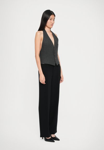 Gilet gris à côtes avec décolleté en V profond et cinq boutons, associé à un pantalon noir taille haute et des escarpins noirs à bout pointu.