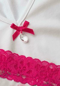 Biała tkanina z głębokim różowym koronkowym wykończeniem na dole, zdobiona małą różową wstążką i przezroczystym akcentem w kształcie kropli w okolicy dekoltu.