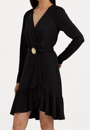 Zwarte jurk met lange mouwen, diepe V-hals, gepofte lijfje en gerimpelde zoom. Heeft een ceintuur met een gouden bloemenaccent. Gladde stof.