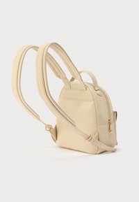Μπεζ μίνι σακίδιο με δομημένο σχήμα, ομαλή υφή, με ρυθμιζόμενους ιμάντες και λεπτομέρεια φερμουάρ σε χρυσή απόχρωση.
