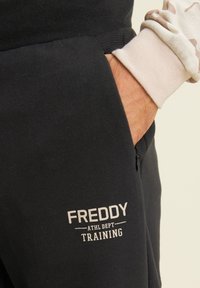 Pantaloni della tuta neri con logo "FREDDY ATHL DEPT TRAINING", dotati di una tasca laterale con zip e una finitura morbida e testurizzata.