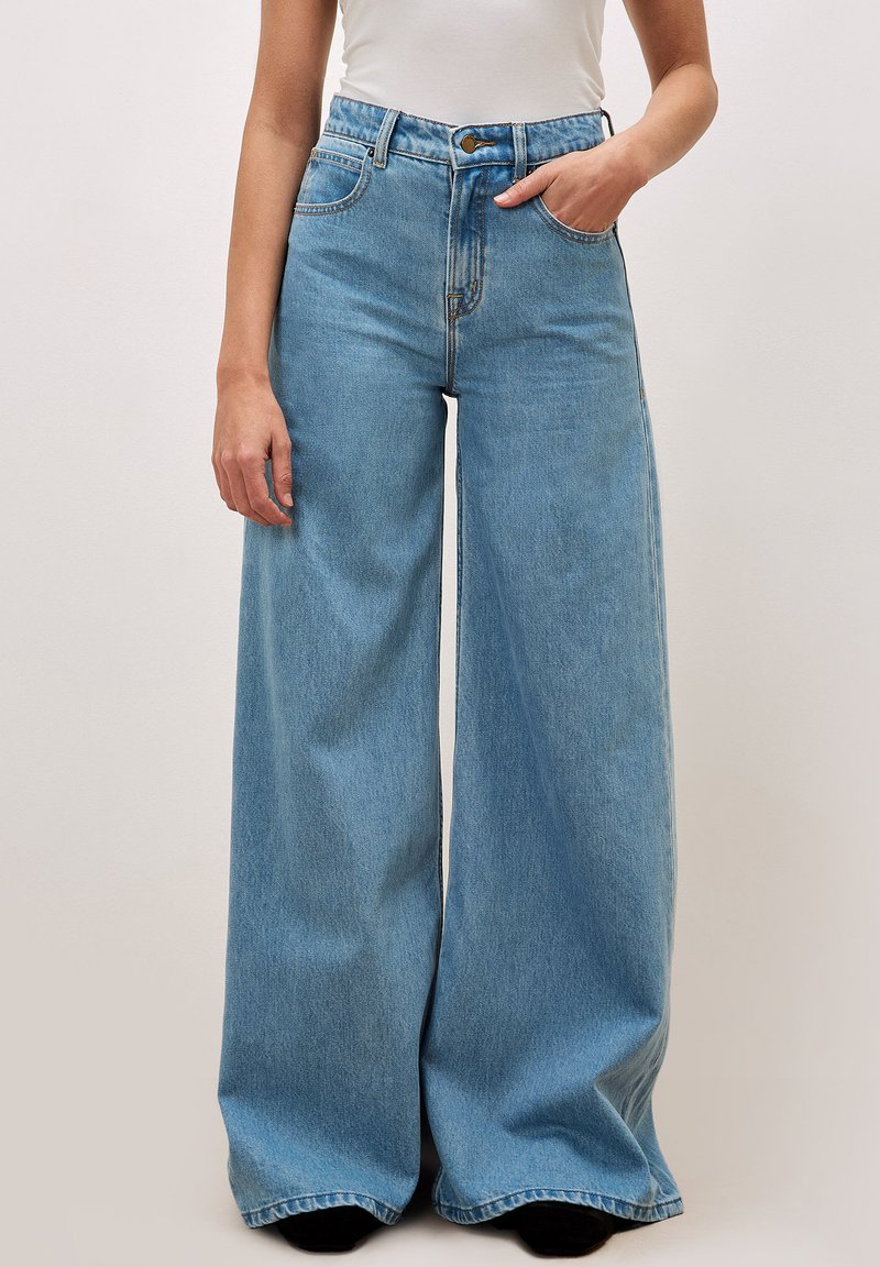 Jean large bleu clair à taille haute, avec poches avant et fermeture à bouton. Fabriqué en denim avec une texture douce et un minimum de détails de couture.
