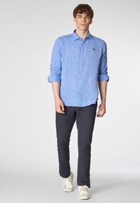 Camicia azzurro chiaro con maniche arrotolate, caratterizzata da una sottile texture. Indossata con pantaloni scuri e sneakers bianche.