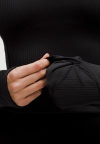 Sort tætsiddende langærmet top med ribbet tekstur og tommelfingerhuller. Stoffet synes strækbart, med diskret sømdetaljering langs manchetterne.