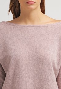 Ljusrosa avbiten tröja med mjukt tyg och avslappnad passform. Har en vid halsringning och subtil textur genom hela plagget.