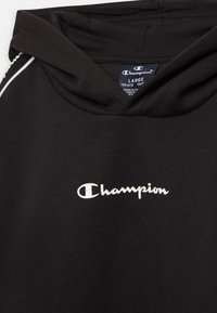 Sudadera con capucha negra hecha de algodón. Presenta un logo blanco de "Champion" en el pecho y costuras en blanco a lo largo de la capucha.