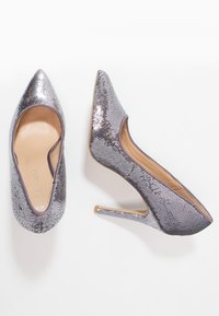 Silverfärgade paljettklackar med spetsig tå, tunn stilettklack och en slät innerfoder. Den texturerade ovansidan ökar den visuella attraktionskraften.