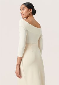 Kreemist off-the-shoulder ribakootud topp kolmeveerandite varrukatega, koos kitsaste kreemidest seelikutega, mis toovad välja sujuva tekstuuri.