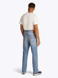Jeans in denim azzurro chiaro con vestibilità rilassata, dotati di una toppa in pelle sul retro, tasche posteriori e un lavaggio leggermente sbiadito. Abbinate a una maglietta bianca.
