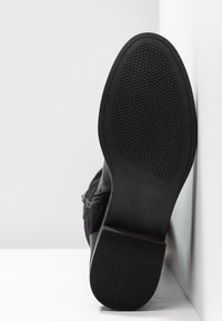 Bottine noire à semelle en caoutchouc texturée, présentant une finition lisse, un détail zippé et un design de talon robuste.