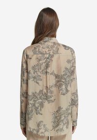 Beige blus med långa ärmar och en intrikat blommönstring i mörkbrunt, med en bakre yoke och en avslappnad passform. Slät, lättvikts tyg.