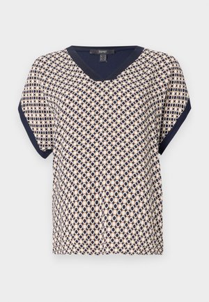 Short-sleeved blouse featuring a navy trim, a V-neck, and a geometric circle pattern in beige and navy hues. Made from a lightweight fabric.