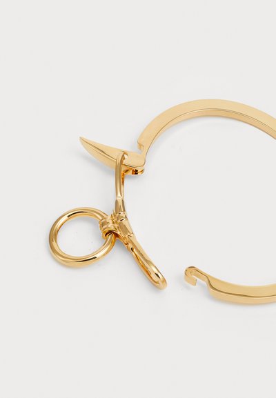 Χρυσόχρωμο μεταλλικό αξεσουάρ με καμπυλωτό σχέδιο, που διαθέτει μία μυτερή άγκυρα, στρογγυλό δαχτυλίδι και λείο φινίρισμα.