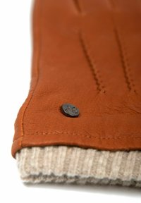 Brown leather item featuring a textured surface, accented with a dark button and a light, ribbed knit fabric at the bottom edge.