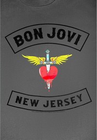 Šedé tričko s černým textem "BON JOVI" a "NEW JERSEY." Uprostřed je grafika srdce s červeným kapajícím efektem, zlatými křídly a mečem.