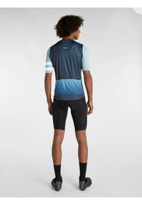 Maillot de cyclisme à manches courtes en bleu foncé et bleu clair, présentant un motif géométrique, et cuissards noirs rembourrés avec une coupe ajustée.