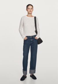 Biały dziergany sweter, ciemnoniebieskie spodnie dzwony z podwiniętymi nogawkami oraz czarne baleriny, uzupełnione brązową torebką z ozdobnym paskiem na ramię z ćwiekami.