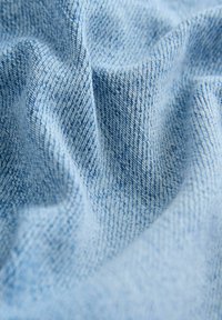 Heledsinine denimpind, millel on tekstuurne kude, nähtavate diagonaalsete mustrite ja pehmete kortsudega, luues voolava väljanägemise.