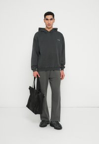 Hallidega hall kapuutsiga sweatshirt, millel on mugav lõige, koos hallide pükstega ja musta õlakotiga. Kanga välimus on pehme ja sile.