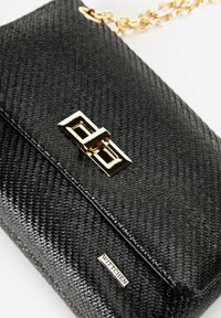 Czarna skórzana kopertówka o teksturowanej powierzchni z złotym prostokątnym zapięciem i łańcuszkowym paskiem, z małą metalową etykietą z logo "WITTCHEN".