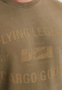 Olijfgroene katoenen sweatshirt met geribbelde halslijn. Wordt gekenmerkt door geprinte tekst in lichtere tinten, waaronder "FLYING LEGENDS" en "CARGO GOODS."