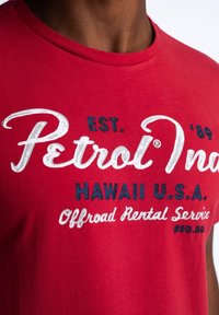 Red cotton t-shirt featuring white and navy graphic text: "Petrol," "Hawaii U.S.A.," and "Offroad Rental Service." Short sleeves, crew neck.