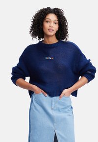 Maglione a maglia navy con una vestibilità boxy e maniche ampie; presenta il logo "Kickers" ricamato in lettere colorate sul petto.