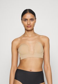 Soutien-gorge sans bretelles nude, sans coutures, avec des coques en mousse et un décolleté plongeant au centre. Texture lisse, design ajusté et aucune quincaillerie visible.