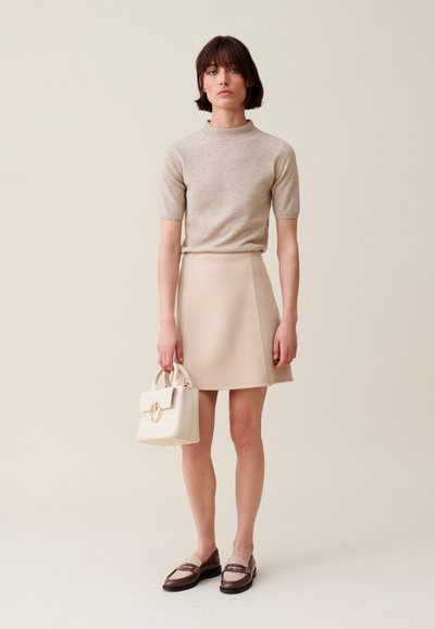 Top de punto de manga corta beige combinado con una falda mini crema, llevando un bolso mini con un acento de anillo dorado. Mocasines marrón y crema completan el look.