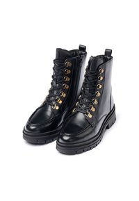 Botas de tobillo de cuero negro con punta redonda, que cuentan con un cierre de cordones en la parte delantera, ojales dorados y una cremallera lateral. Suela de goma gruesa para mayor tracción.