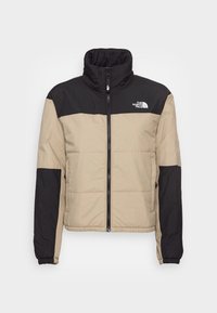 Puffjacka med hög krage, med en tanfärgad kropp och svarta ärmar. Dragkedjestängning och The North Face-logotyp på övre vänstra sidan.
