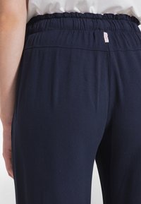 Granatowe spodnie z elastycznym pasem. Miękki, elastyczny materiał o gładkiej fakturze. Z tyłu znajduje się mała metka.