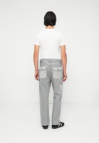 Pantaloni gri cu picioare drepte, cu un finisaj texturat, două buzunare la spate și un buzunar cargo pe lateral, purtați cu un tricou alb simplu și sandale.