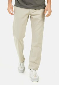Lys beige, lige ben-pants lavet af blødt stof. Har et enkelt design med minimale syninger. Parret med hvide sneakers.