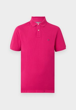 Polo rose vif à manches courtes avec patte à deux boutons et petit logo rectangulaire sur la poitrine gauche sur fond uni.