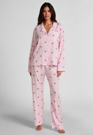 Hellrosa Schlafanzug-Set aus weichem Stoff, bestehend aus einem Oberteil mit Knöpfen, einer Tasche und langen Ärmeln, kombiniert mit passenden locker sitzenden Hosen, die mit kleinen roten Blumen verziert sind.