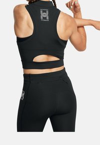 Czarny sportowy crop top z wycięciem i logo na plecach, zestawiony z czarnymi legginsami z wysokim stanem, które mają kieszeń na zamek i akcenty logo.