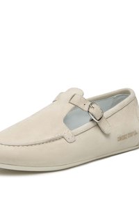 Scarpa slip-on in suede beige con design a intaglio, dettaglio fibbia in argento, cuciture e una morbida fodera interna. Marchio Cultured Cooper presente.