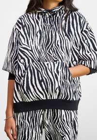 Sudadera de rayas zebra en blanco y negro con un bolsillo frontal, mangas anchas y capucha con cordón. Tejido suave y detalle en el dobladillo acanalado.