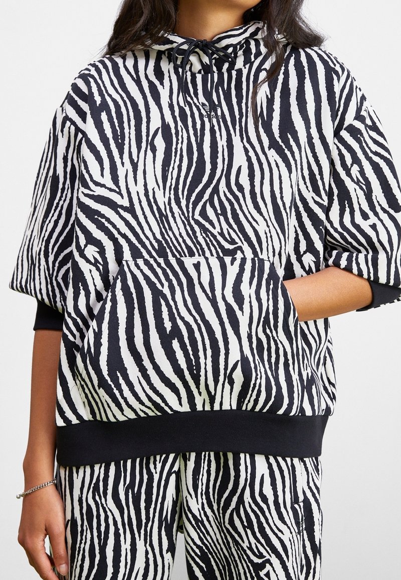 Sudadera de rayas zebra en blanco y negro con un bolsillo frontal, mangas anchas y capucha con cordón. Tejido suave y detalle en el dobladillo acanalado.
