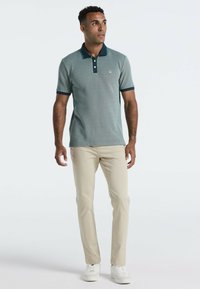 Polo shirt in teal met korte mouwen, een kraag en donkere accenten. Gecombineerd met lichtbeige broek en witte sneakers met een gestructureerd patroon.