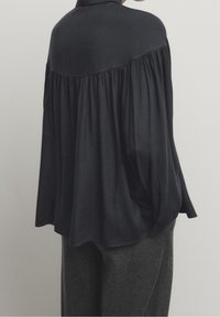 Vloeiende zwarte blouse met een geplooide achterkant, taps toelopende mouwen en een ontspannen pasvorm. Gemaakt van zachte stof met een gladde textuur.