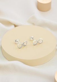 Silverhängen som har en oändlighetssymbol-design, slät yta och säker fäste, visade på en rund beige podium.