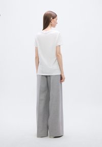 Λευκό κοντομάνικο μπλουζάκι συνδυασμένο με γκρι παντελόνι φαρδιάς γραμμής. Το ύφασμα φαίνεται λείο, με χαλαρή εφαρμογή και ελάχιστες λεπτομέρειες.