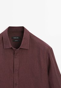Burgundská lněná košile s klasickým límcem, knoflíkovým zapínáním a texturovaným povrchem. Obsahuje značkovou etiketu uvnitř límce.