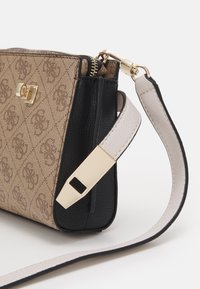 Brun og sort crossbody-taske med gulddetaljer, med et struktureret stofmønster og en glat læderrem. Lynlåslukning synlig.