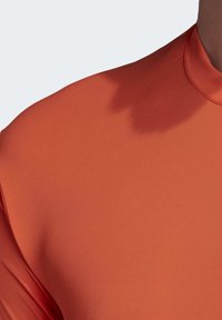 Orange atletisk skjorte med høj hals, korte ærmer og et glat, tekstureret stof. Designet fremhæver en moderne pasform.