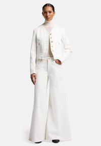 Witte denim cropped jack met gouden knopen en twee voorzakken, gecombineerd met brede witte broeken en een crème turtleneck.
