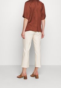 Brown kort mouwtop met een Gathering halslijn, gecombineerd met crèmekleurige wijde broek en bruine hoge sandaaltjes, gezien vanuit de achterkant.
